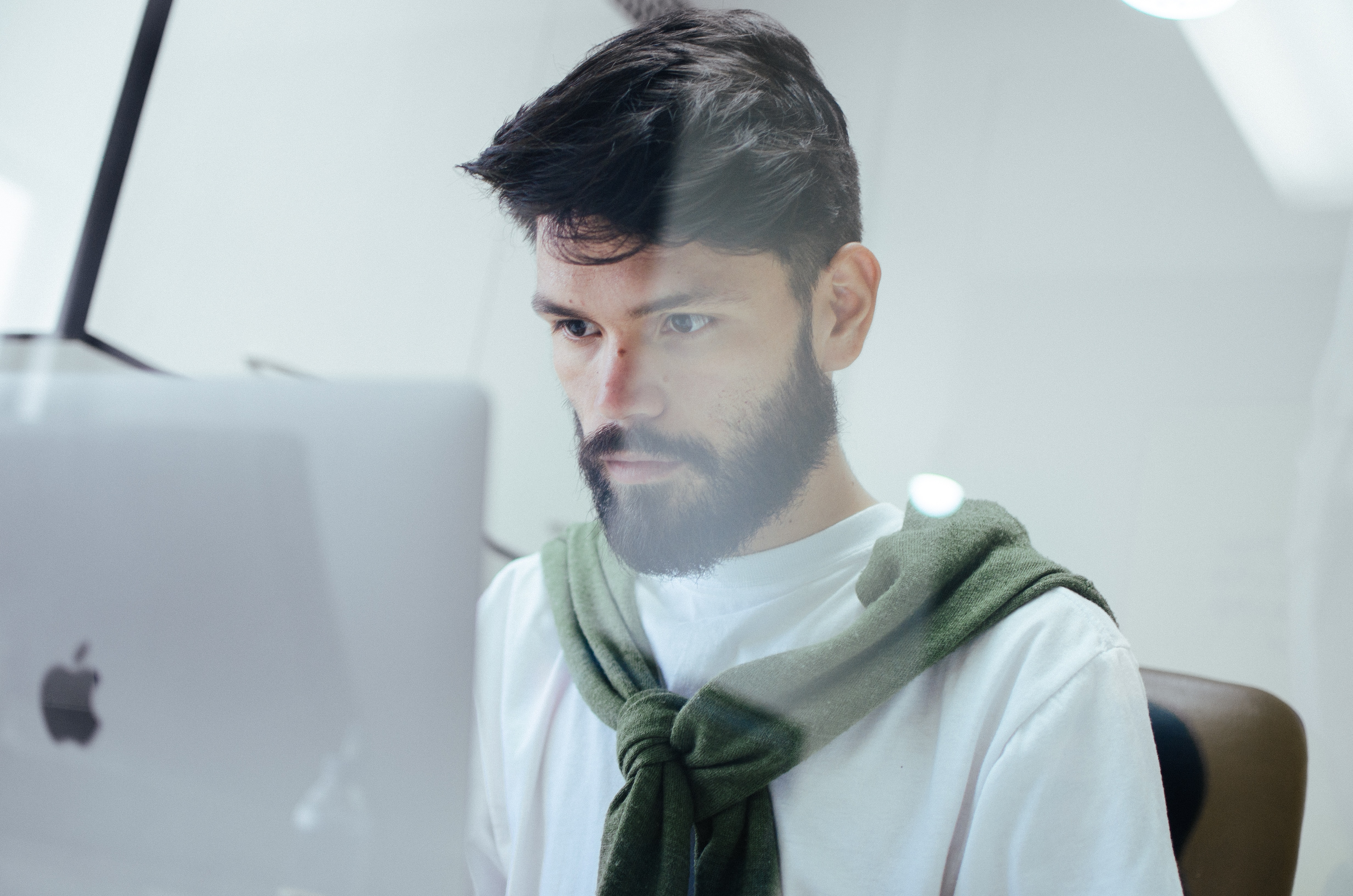 Man with short, dark hair sitting at a desk working on an Apple laptop computer.