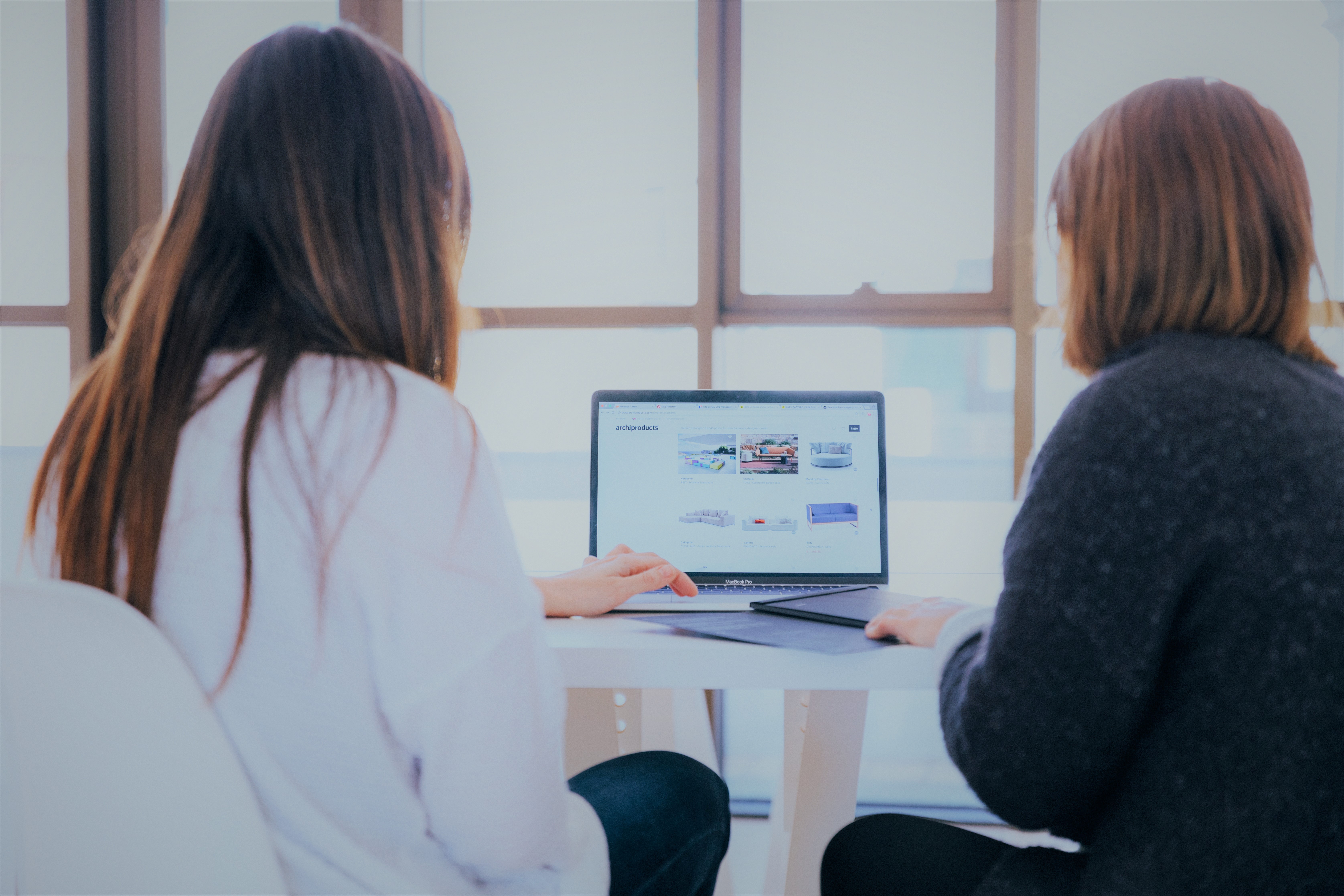 Two women sitting at a desk working together on a laptop.